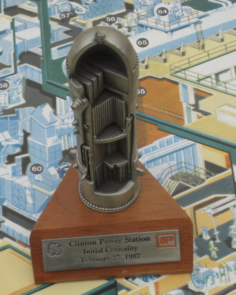 Cutaway model of a General Electric BWR-6 nuclear power reactor, mounted on a wooden plinth, with a plaque reading "Clinton Power Station Initial Criticality February 27, 1987".