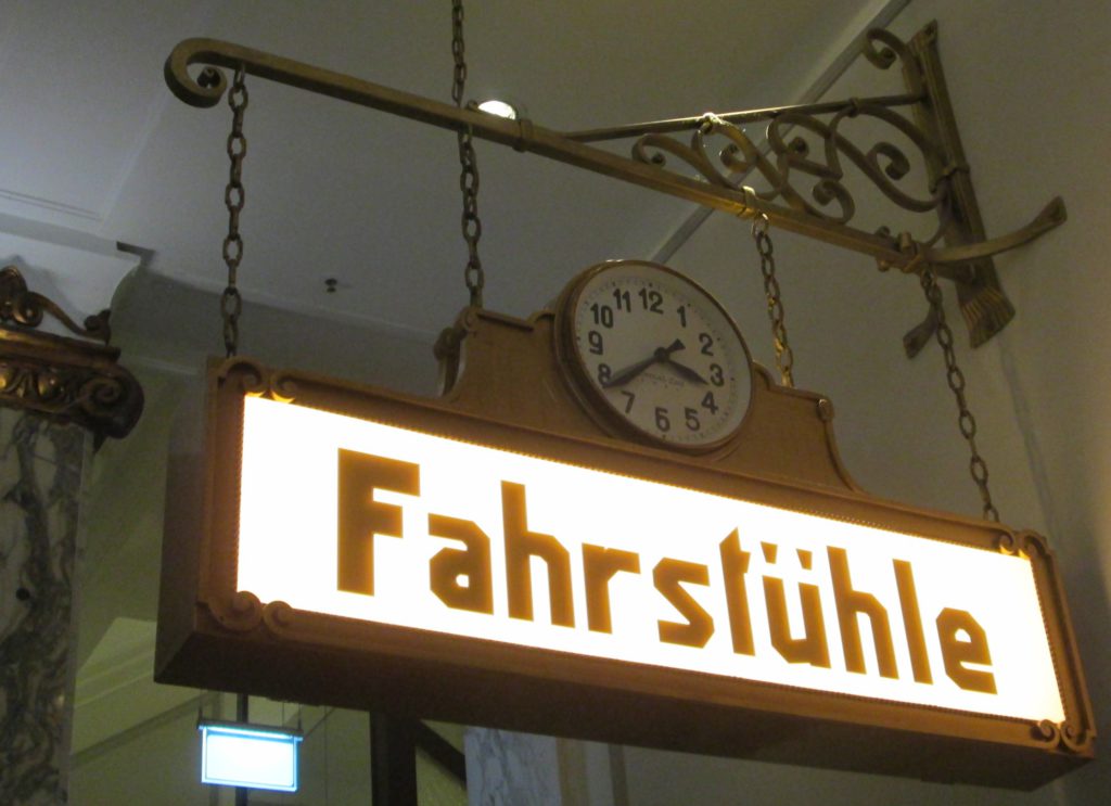 An ornate illuminated sign with the German text "Fahrstühle", also incorporating a clock